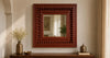 Hand-carved wooden wall mirror mounted above a solid wood console in a warm neutral interior, featuring intricate traditional detailing and a rich brown finish.