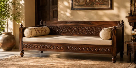 Hand-carved sheesham wood diwan with diamond pattern carving and traditional cushions in an Indian living room