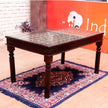 Wooden table with glass top on a patterned rug, with an orange wall in the background