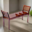 Wooden bench with slatted design on a concrete floor.