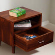 Wooden side table with open drawer containing books and magazines, on a plain background.