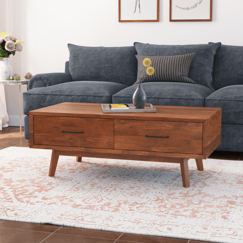 Wooden coffee table in front of a gray sofa with decorative items on a white rug.
