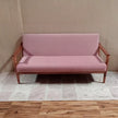 Pink sofa with wooden frame against a beige wall.