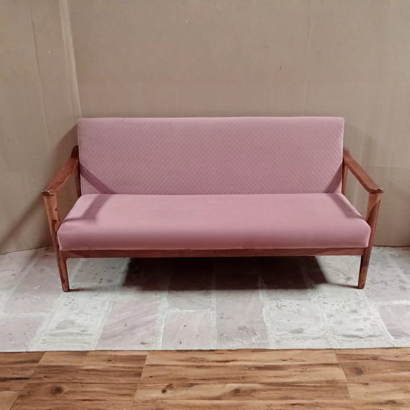 Pink sofa with wooden frame against a beige wall.