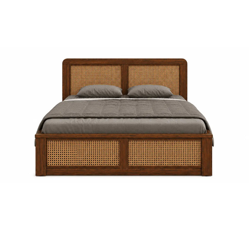 A wooden platform bed with a dark brown finish and woven cane panels on the headboard and footboard, dressed in a gray quilt and two gray pillows, shown against a plain white background.