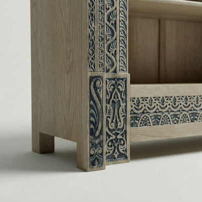 Closeup view of Meher rustic teak wood hand-carved display cabinet emphasizing light wood shelves and carved pedestal base