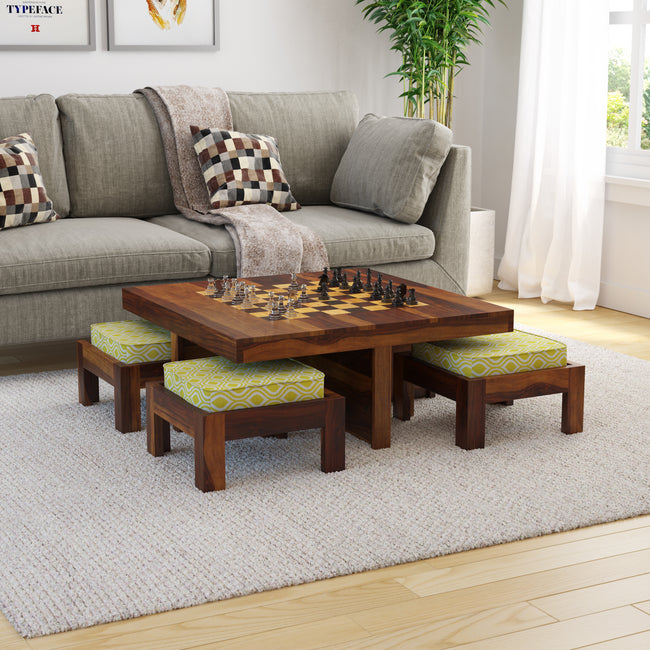 A sheesham wood chess coffee table set with 4 stools in a living room setting, the table displaying a chessboard and the stools having green and yellow fabric covers.